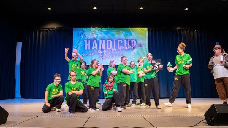 Mehrere Jugendliche mit Downsyndrom stehen in grünen T-Shirts auf einer Bühne mit zwei Erwachsenen. (Foto: SWR) Mehrere Jugendliche mit Downsyndrom stehen in grünen T-Shirts auf einer Bühne mit zwei Erwachsenen.