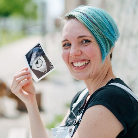 Tanja zeigt lachend ein Ultraschallbild ihres Kindes