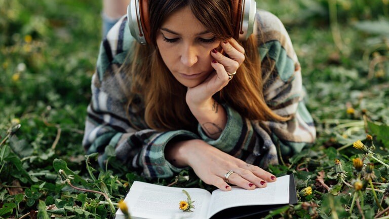 Eine Frau liegt lesend auf einer Wiese. Ein gutes Buch lesen macht den Urlaub perfekt. SWR1 verrät, welche Bücher an Pfingsten oder bei der Reise im Sommer 2023 mit dabei sein müssen. (Foto: picture-alliance / Reportdienste, Picture Alliance)