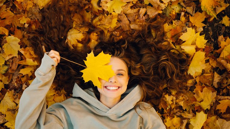 Eine Frau liegt lachend im Herbstlaub. (Foto: picture-alliance / Reportdienste, picture alliance / Zoonar | Max 4e)