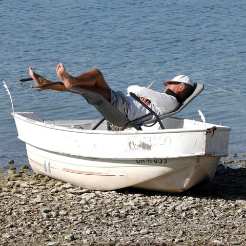 Weil der Liegestuhl auf dem steinigen Untergrund wackelt, hat der Mann diesen in das am Ufer liegende Boot gestellt. (Foto: picture-alliance / Reportdienste, picture alliance / Jochen Eckel | Jochen Eckel)