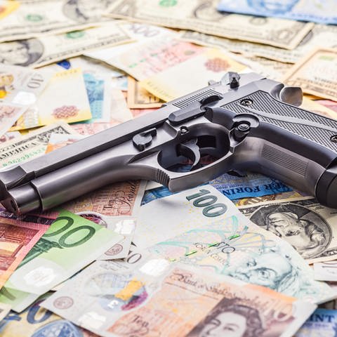 Handgun on the various banknotes background. (Foto: picture-alliance / Reportdienste, picture alliance / Zoonar | Jiri HERA)