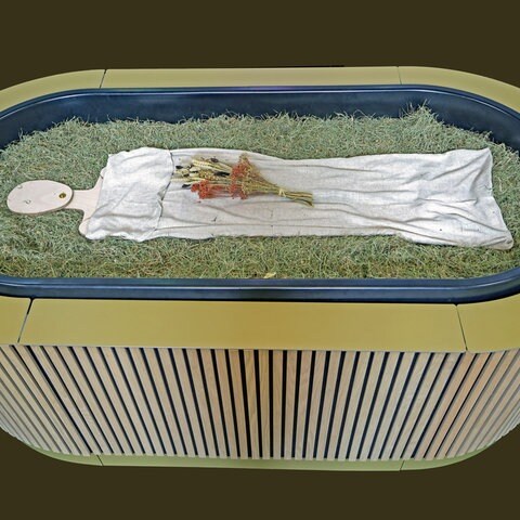Heu, Stroh, Blumen und eine Holzfigur liegen in einem sogenannten „Kokon“ bei einem Pressegespräch zu der neuen Bestattungsform "Reerdigung" in der Kapelle auf dem Parkfriedhof Eichhof. Der Anbieter „Meine Erde“ bietet die neuen Bestattungsform an. Ein Leichnam wird auf Heu, Stroh und Grünschnitt gebettet, innerhalb von 40 Tagen wird er zu Erde. (Foto: dpa Bildfunk, picture alliance/dpa | Christian Charisius)