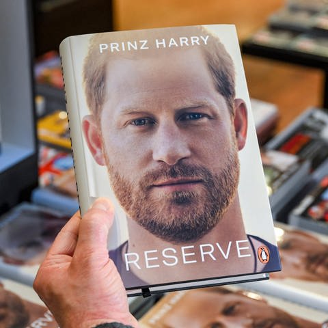 Eine Hand hält die Biografie "Reserve" von britischen Königssohn Prinz Harry in der Hand. (Foto: dpa Bildfunk, Picture Alliance)