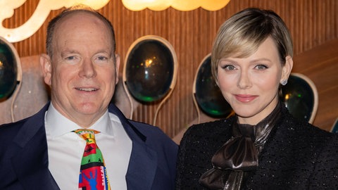 Fürstin Charlène von Monaco und Fürst Albert von Monaco sind beide schick gekleidet und lächeln auf einem Portrait-Foto in die Kamera. Er hat eine bunte Krawatte zu einem blauen Anzug mit weißem Hemd, während sie in elegantem schwarz gekleidet ist, mit hochgeschlossenem Kragen. (Foto: IMAGO, xVinajx-xPoolxCrystalx/xStarfacex STAR_303437_038) Fürstin Charlène von Monaco und Fürst Albert von Monaco sind beide schick gekleidet und lächeln auf einem Portrait-Foto in die Kamera. Er hat eine bunte Krawatte zu einem blauen Anzug mit weißem Hemd, während sie in elegantem schwarz gekleidet ist, mit hochgeschlossenem Kragen.