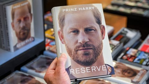 Eine Hand hält die Biografie "Reserve" von britischen Königssohn Prinz Harry in der Hand. (Foto: dpa Bildfunk, Picture Alliance) Eine Hand hält die Biografie "Reserve" von britischen Königssohn Prinz Harry in der Hand.