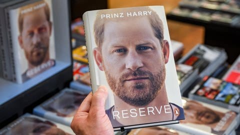 Eine Hand hält die Biografie "Reserve" von britischen Königssohn Prinz Harry in der Hand. (Foto: dpa Bildfunk, Picture Alliance)