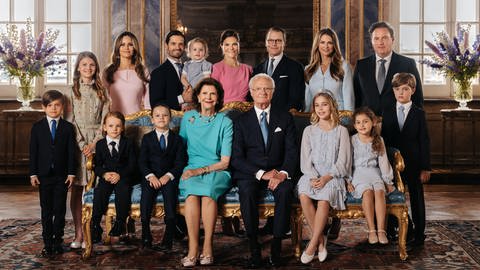 Das Familienfoto der schwedischen Königsfamile zum 50. Thronjibiläum von König Carl Gustaf von Schweden. Auf dem Foto zu sehen sind neben den drei Kindern des Königs und ihren Partnern auch seine Enkel und natürlich seine Frau Silvia. Sie tragen alle schicke Kleider oder Anzüge und stehen entsprechend angeordnet in einem königlichen Zimmer mit schönen Zierpflanzen. (Foto: Pressestelle, Photo: Clément Morin/The Royal Court of Sweden)