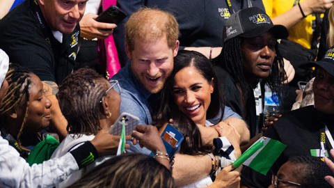 Prinz Harry, Herzog von Sussex, und seine Frau Meghan, Herzogin von Sussex, schauen sich bei den 6. Invictus Games in der Merkur Spiel-Arena zwischen Fans aus Nigeria und der Ukraine Sitzvolleyball der beiden Teams an. Der paralympische Wettbewerb für kriegsversehrte Sportler ist erstmals in Deutschland zu Gast. (Foto: dpa Bildfunk, Picture Alliance)