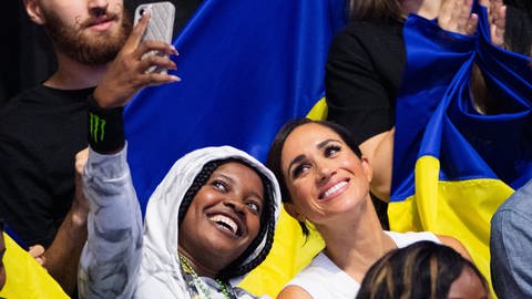 Meghan, Herzogin von Sussex, schaut sich bei den 6. Invictus Games in der Merkur Spiel-Arena zwischen Fans aus Nigeria und der Ukraine Sitzvolleyball der beiden Teams an und macht ein Selfie mit einem nigerianischen Fan. Der paralympische Wettbewerb für kriegsversehrte Sportler ist erstmals in Deutschland zu Gast. (Foto: dpa Bildfunk, Picture Alliance)