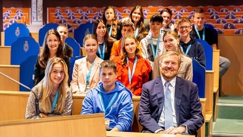 König Willem-Alexander bei "Pro Demos" in Den Haag: Der niederländische König sitzt zusammen mit jungen Studierenden in einem Hörsaal und lächelt in die Kamera. (Foto: picture-alliance / Reportdienste, ROBIN UTRECHT)