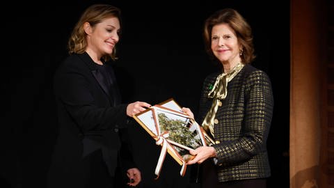 Es stehen zwei Frauen schräg gegenüber, die eine etwas älter hält ein Bild in der Hand und lächelt (Foto: picture-alliance / Reportdienste, Picture Alliance) Es stehen zwei Frauen schräg gegenüber, die eine etwas älter hält ein Bild in der Hand und lächelt