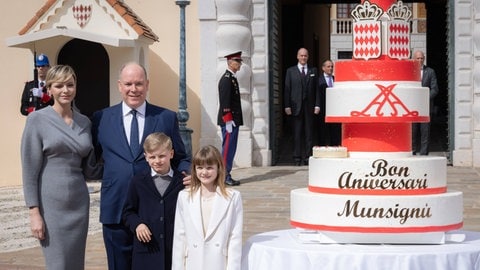 Fürst Albert von Monaco mit Fürstin Charlène von Monaco stehen mit ihren Kindern Prinz Jacques und Prinzessin Gabriella vor dem Palast in Monaco und lächeln wie auf einem perfekten Familienfoto. Neben ihnen steht eine menschengroße Torte mit einem Muster wie auf dem monegassischen Fürstenwappen in rot und weiß. Charlene trägt ein graues eng anliegendes knielanges Kleid, Gabriella einen weißen Blazer und die Männer sind in dunkelblau gekleidet. (Foto: IMAGO, IMAGO Starface xVinajx-xPoolxCrystalx/xStarfacex STAR_302775_010) Fürst Albert von Monaco mit Fürstin Charlène von Monaco stehen mit ihren Kindern Prinz Jacques und Prinzessin Gabriella vor dem Palast in Monaco und lächeln wie auf einem perfekten Familienfoto. Neben ihnen steht eine menschengroße Torte mit einem Muster wie auf dem monegassischen Fürstenwappen in rot und weiß. Charlene trägt ein graues eng anliegendes knielanges Kleid, Gabriella einen weißen Blazer und die Männer sind in dunkelblau gekleidet.