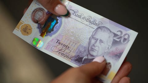Ein Mensch mit rosa Nagellack hält eine 20-er Banknote in den Händen. Darauf ist König Charles abgebildet. (Foto: dpa Bildfunk, Picture Alliance) Ein Mensch mit rosa Nagellack hält eine 20-er Banknote in den Händen. Darauf ist König Charles abgebildet.