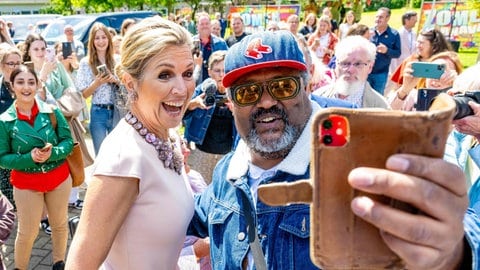 Links steht Maxima im rosa-weißen Kostüm mit einer klobigen Kette um den Hals und strahlt mit offenem Mund in ein Smartphone, das von einem Mann mit Kappie rechts neben ihr für ein Selfie gehalten wird (Foto: picture-alliance / Reportdienste, Picture Alliance) Links steht Maxima im rosa-weißen Kostüm mit einer klobigen Kette um den Hals und strahlt mit offenem Mund in ein Smartphone, das von einem Mann mit Kappie rechts neben ihr für ein Selfie gehalten wird