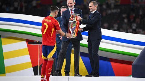 Fußballer Alvaro Morata (l-r) bekommt nach dem EM-Sieg die Trophäe von König Felipe von Spanien und vom UEFA-Präsident Aleksander Ceferin überreicht. (Foto: dpa Bildfunk, picture alliance/dpa | Tom Weller) Fußballer Alvaro Morata (l-r) bekommt nach dem EM-Sieg die Trophäe von König Felipe von Spanien und vom UEFA-Präsident Aleksander Ceferin überreicht.