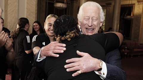 König Charles III. trifft die neuseeländische Rugby-Union-Mannschaft der Black Ferns im Buckingham Palace in London, umarmt eine Spielerin und hat dabei die Augen geschlossen. (Foto: picture-alliance / Reportdienste, picture alliance / empics | Aaron Chown) König Charles III. trifft die neuseeländische Rugby-Union-Mannschaft der Black Ferns im Buckingham Palace in London, umarmt eine Spielerin und hat dabei die Augen geschlossen.