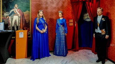 Links steht Prinzessin Amalia der Niederlande in einem royalblauen langen Kleid mit Krone, rechts daneben Königin Máxima auch in einem langen royalblauen Kleid mit Krone und ganz rechts König Willem-Alexander im schwarzen Wrack mit Schärpe (Foto: picture-alliance / Reportdienste, Picture Alliance) Links steht Prinzessin Amalia der Niederlande in einem royalblauen langen Kleid mit Krone, rechts daneben Königin Máxima auch in einem langen royalblauen Kleid mit Krone und ganz rechts König Willem-Alexander im schwarzen Wrack mit Schärpe