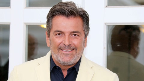 Schlagersänger Thomas Anders steht in einem weißen Anzug vor einer weißen Tür und lächelt in die Kamera. (Foto: picture-alliance / Reportdienste, picture alliance / Geisler-Fotopress | gbrci/Geisler-Fotopress)