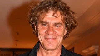Wolfgang Maria Bauer trägt eine schwarze Weste und lacht direkt in die Kamera