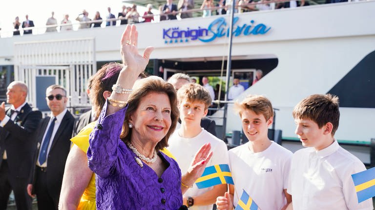 Königin Silvia von Schweden winkt vor dem Schiff der Weißen Flotte bei einer Benefizveranstaltung zugunsten der World Childhood Foundation. (Foto: dpa Bildfunk, Picture Alliance)