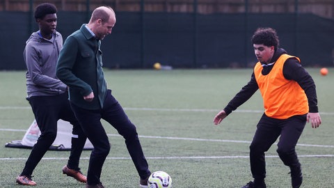 Prinz William spielt Fußball gegen zwei Jugendliche bei einem Besuch eines Gemeinschaftszentrums in Liverpool. (Foto: picture-alliance / Reportdienste, picture alliance/dpa/PA Wire | Temi Adelaja) Prinz William spielt Fußball gegen zwei Jugendliche bei einem Besuch eines Gemeinschaftszentrums in Liverpool.