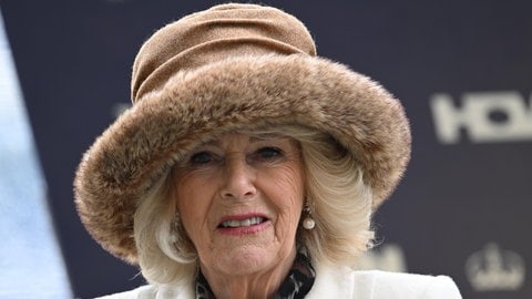 Eine ältere Frau mit blondem Haar und einem großen, hellbraunen Hut mit Kunstfellrand lächelt in die Kamera. Queen Camilla trägt einen hellen Mantel mit Hufeisenbrosche. (Foto: picture-alliance / Reportdienste, Sipa USA | Focus Images) Eine ältere Frau mit blondem Haar und einem großen, hellbraunen Hut mit Kunstfellrand lächelt in die Kamera. Queen Camilla trägt einen hellen Mantel mit Hufeisenbrosche.