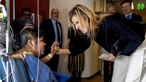 Eine blonde langhaaringe Frau, Königin Máxima, beugt sich zu einer Patientin im Rollstuhl, lächelt sie an und drückt ihre Hand. (Foto: picture-alliance / Reportdienste, abaca | Bruno Press/ABACA) Eine blonde langhaaringe Frau, Königin Máxima, beugt sich zu einer Patientin im Rollstuhl, lächelt sie an und drückt ihre Hand.