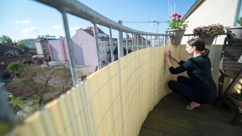 Eine Frau befestigt an ihrem Balkon einen Sichtschutz (Foto: picture-alliance / Reportdienste, Andrea Warnecke/dpa-tmn) Eine Frau befestigt an ihrem Balkon einen Sichtschutz
