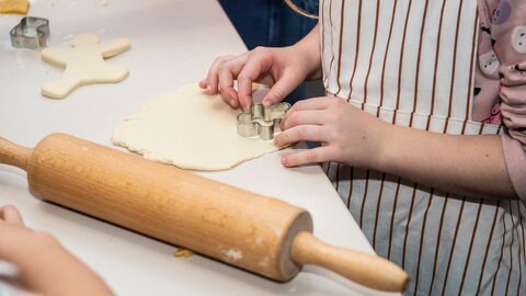 Wellholz neben ausgewellten Salzteig, in dem ein Kind Ausstecher drückt: Zum Herstellen und Trocknen von Deko kann man wie beim Plätzchenbacken vorgehen. (Foto: IMAGO, IMAGO / Funke Foto Services)