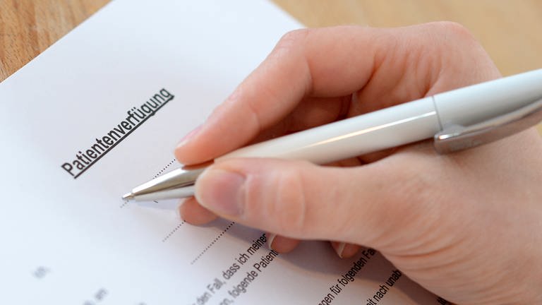 Patientenverfügung richtig ausfüllen: Eine Hand mit einem Stift setzt auf einem Vordruck zum Schreiben an. (Foto: dpa Bildfunk, Picture Alliance)