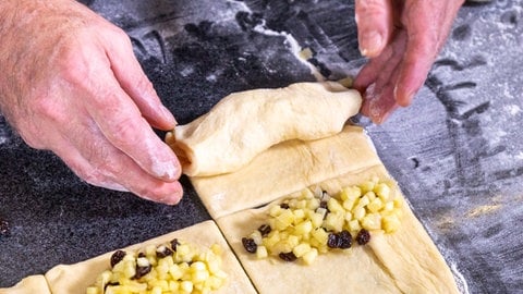 Die Apfel-Karamell-Füllung kommt auf den ausgerollten Hefeteig, dann rollt Joachim Habiger ihn zu den Apfeltaschen zusammen. (Foto: SWR, Corinna Holzer) Die Apfel-Karamell-Füllung kommt auf den ausgerollten Hefeteig, dann rollt Joachim Habiger ihn zu den Apfeltaschen zusammen.