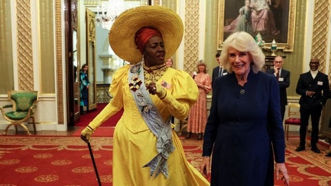 Links geht eine Frau in einem gelben Kostüm mit Hut durch den Buckingham Palace, begleitet von rechts daneben der blonden Königin Camilla in dunklem Kleid. Sie unterhalten sich. (Foto: picture-alliance / Reportdienste, empics | Isabel Infantes) Links geht eine Frau in einem gelben Kostüm mit Hut durch den Buckingham Palace, begleitet von rechts daneben der blonden Königin Camilla in dunklem Kleid. Sie unterhalten sich.