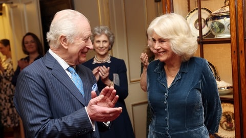 Links steht König Charles im Anzug und klatscht für Königin Camilla, die rechts im dunkelblauen Kleid steht. Beide strahlen übers ganze Gesicht. (Foto: picture-alliance / Reportdienste, ASSOCIATED PRESS | Chris Jackson) Links steht König Charles im Anzug und klatscht für Königin Camilla, die rechts im dunkelblauen Kleid steht. Beide strahlen übers ganze Gesicht.