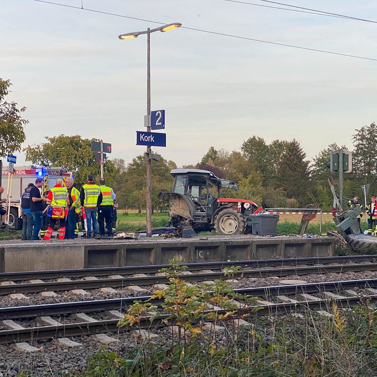 Ein beschädigter Traktor und Rettungskräfte stehen am Bahnhof Kork, einem Stadtteil von Kehl. Laut Polizei ist der Traktor auf dem Bahnübergang liegengeblieben. Ein TGV-Zug konnte den Angaben nach nicht mehr rechtzeitig bremsen und ist mit dem Traktor zusammengestoßen. 