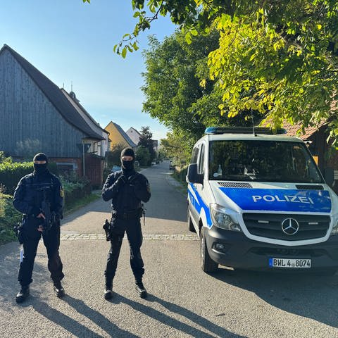 Zwei Polizisten des SEK stehen neben einem Polizeiauto im Ortsteil Hesselbronn.