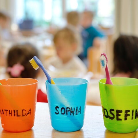 Kinder sitzen vor Zahnbürsten und Zahnputzbechern (Foto: dpa Bildfunk, picture alliance/dpa/Monika Skolimowska (Symbolbild))