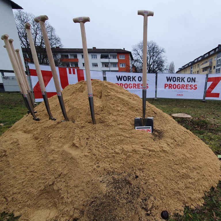 Spaten stecken in Sandhaufen vor Häuserblock in Konstanz