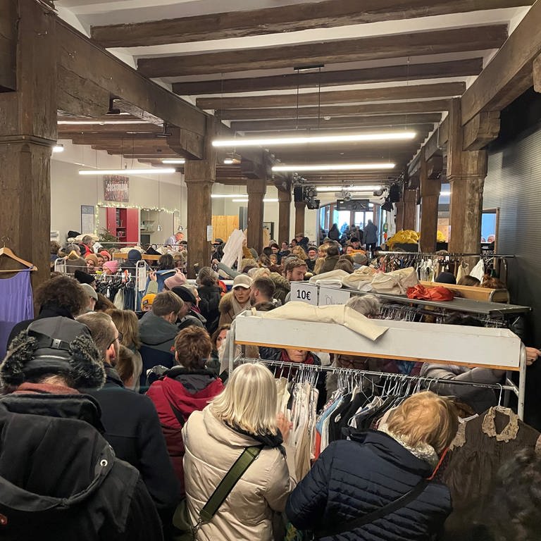 Besucher des Kostuemverkaufs des Theater Konstanz stöbern in den Sachen und zeigen ihre Fundstücke wie ein gestreiftes Jacket oder einen übergroßen Mantel aus dem Weihnachtsmärchen