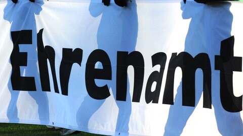 Drei Personen halten ein Schild mit der Aufschrift "Ehrenamt" (Foto: dpa Bildfunk, picture alliance/dpa | Patrick Seeger)