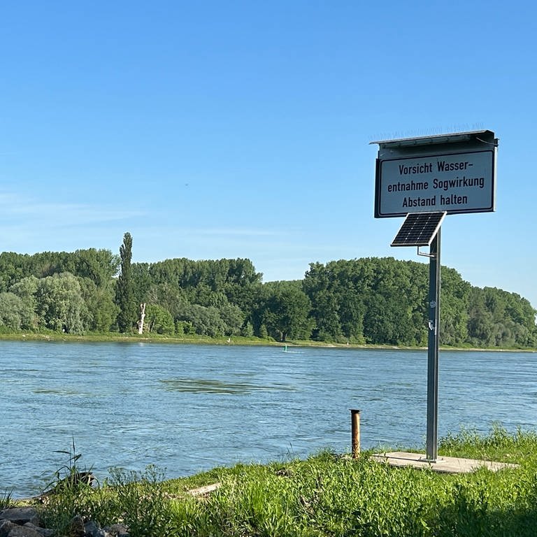 Blick über der Rhein bei Karlsruhe. Am Rand steht ein Schild, das vor Sogwirkung wegen Wasserentnahme warnt. 