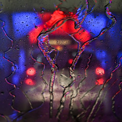 Wasser perlt an der Frontscheibe eines Pkw ab, der durch eine in rotes und blaues Licht getauchte Waschanlage fährt. (Foto: dpa Bildfunk, picture alliance/dpa | Arne Dedert)
