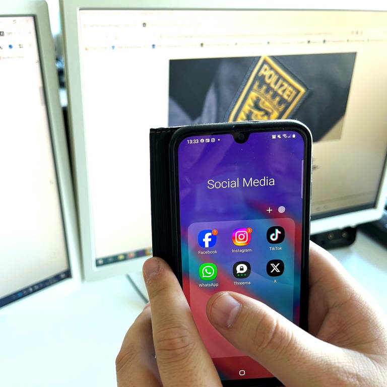 Symbolbild Faktencheck: Eine Hand mit Handy mit Social Media Apps vor einem Bildschirm. 