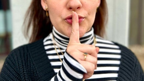 Eine Frau hebt ihren Zeigefinger vor den Mund.