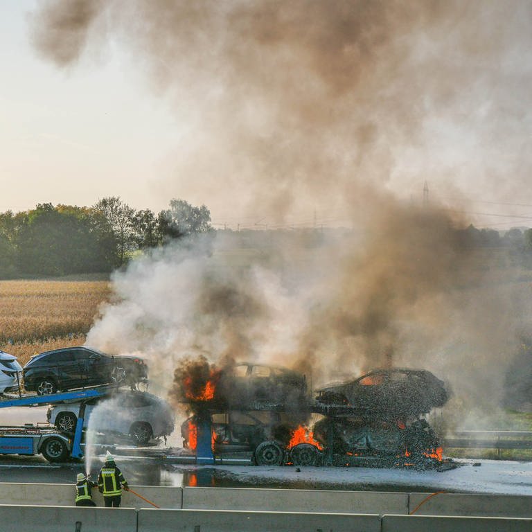 Einsatzkräfte der Feuerwehr löschen in Brand geratene Autos auf einem Transporter. 