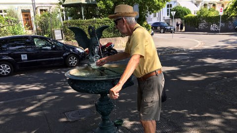 ein Mann erfrischt sich an einem Brunnen 