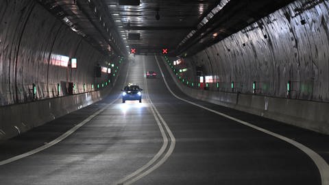Zu sehen ist ein Tunnel. Er ist relativ dunkel, ein Auto fährt auf uns zu. Das einzige Licht scheint von dessen Scheinwerfern zu kommen. 