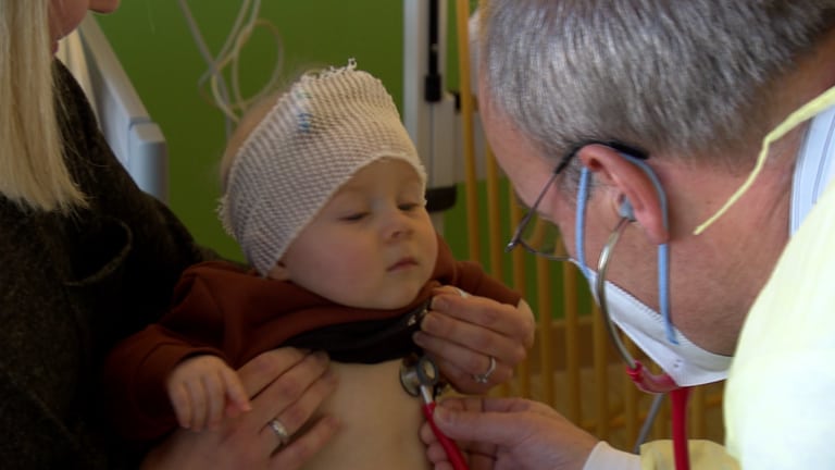 Der sechs Monate alte Fiete sitzt auf dem Schoß seiner Mutter, während ein Arzt ihn abhört. 