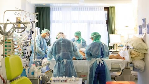 Mehrere Ärzte und Pfleger stehen am Krankenbett in der Klinik. Ein an Corona erkrankter Patient wird im Februar 2021 auf einer Intensivstation im Uniklinikum Tübingen behandelt. 
