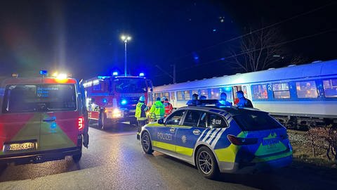 Mehrere Rettungs- und Streifenwagen stehen am späten Abend in der Dunkelheit vor einem Zug. Eine 39-jährige Frau ist am Montag auf der Riesbahn zwischen Nördlingen und Aalen von einem Zug mehrere Kilometer mitgeschleift worden.
